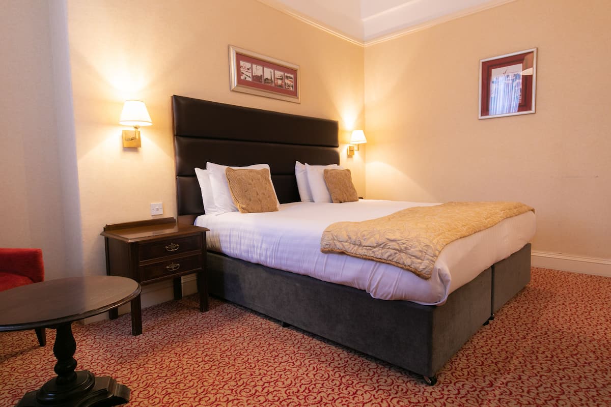 A neatly arranged hotel room with a large bed, two bedside tables, a small table, and a red chair.