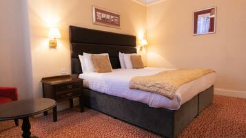 A neatly arranged hotel room with a large bed, two bedside tables, a small table, and a red chair.