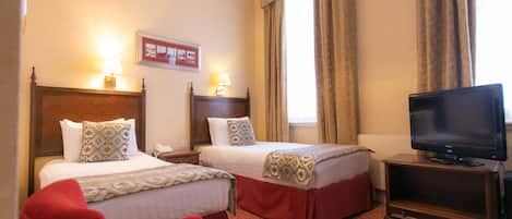 A hotel room with two beds, a TV on a wooden stand, and a red chair.