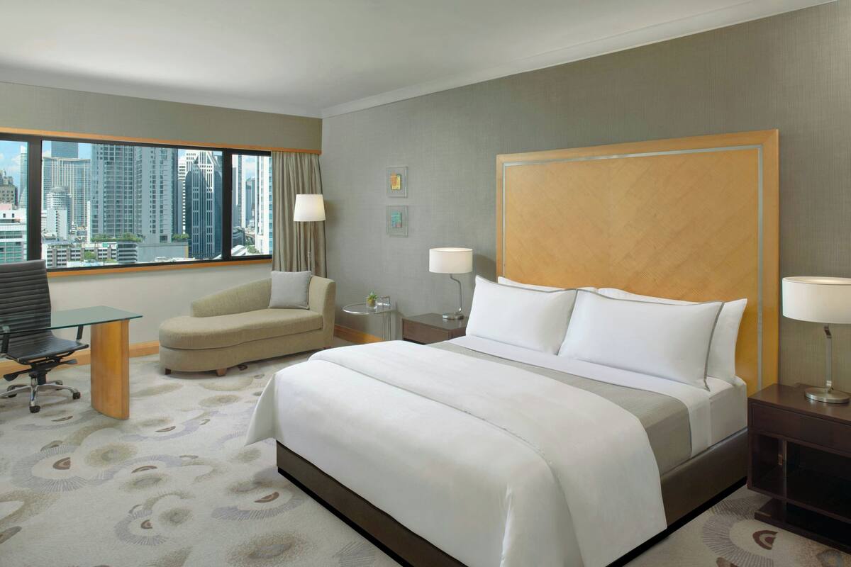 Ein Hotelzimmer mit einem großen Bett, einem Schreibtisch, einem Sessel und Blick auf die Stadt.