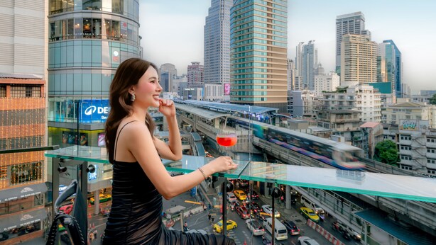 Una mujer en un balcón con vistas a la ciudad, sosteniendo una bebida.
