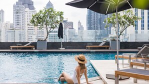 Une femme est assise au bord d’une piscine, avec une vue sur la ville en arrière-plan.
