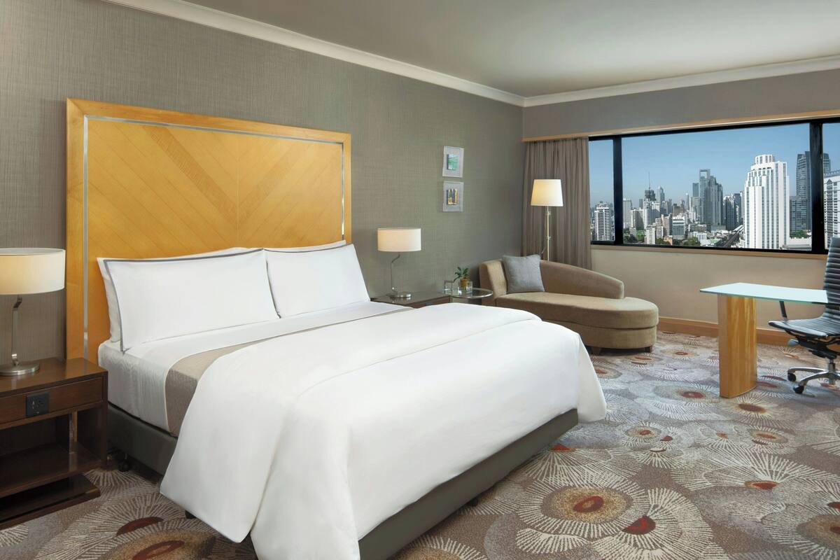 Ein Hotelzimmer mit einem großen Bett, einem Schreibtisch, einem Stuhl und Blick auf die Stadtlandschaft.