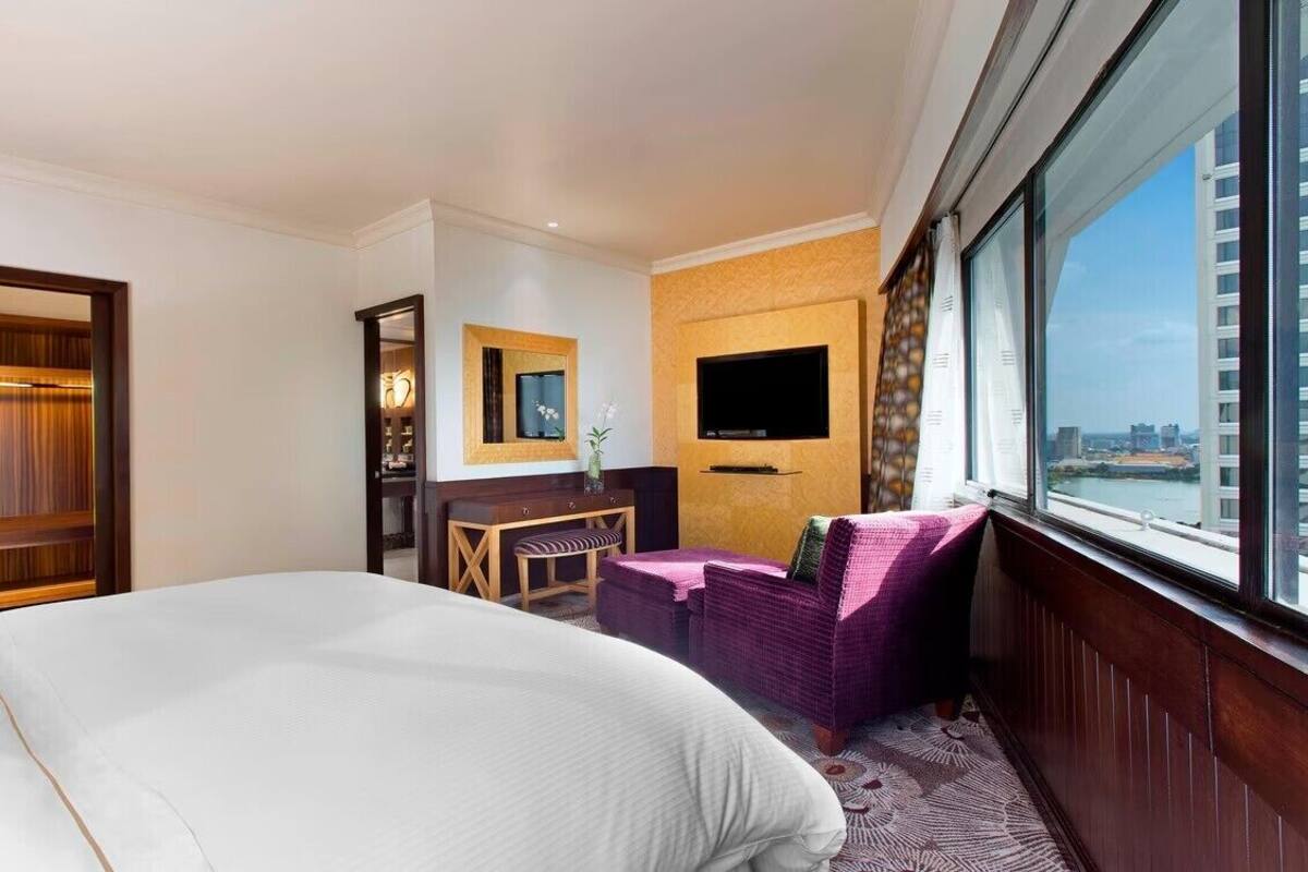 Ein Hotelzimmer mit einem großen Bett, einer Sitzecke mit Fernseher und Blick auf die Stadt durch das Fenster.