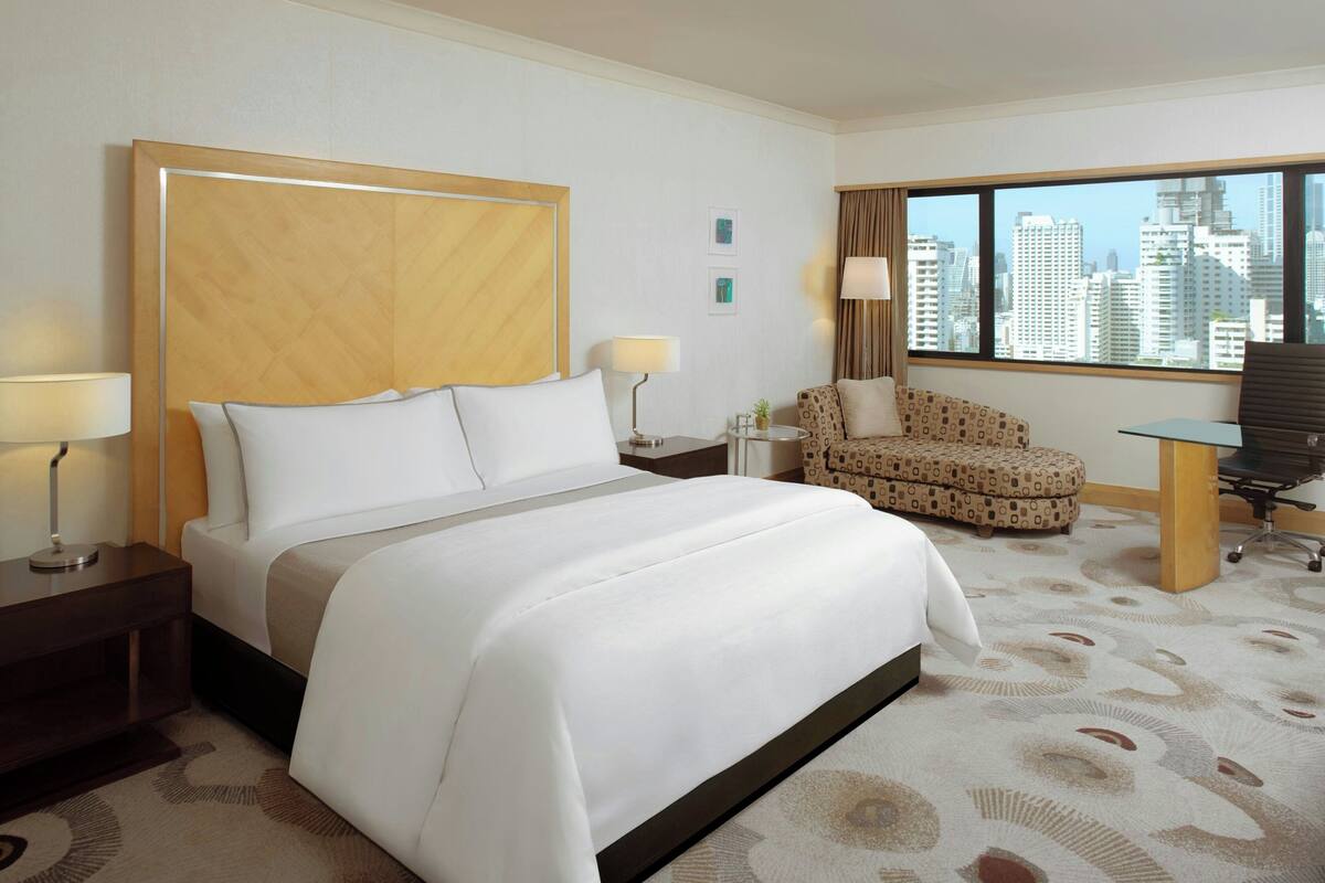 Ein Hotelzimmer mit einem großen Bett, einem Schreibtisch, einem Stuhl und Blick auf die Stadtlandschaft.