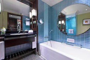 Ein modernes Badezimmer mit einer großen Badewanne, einem Waschtisch inklusive Spiegel und blautonierten Fliesen.