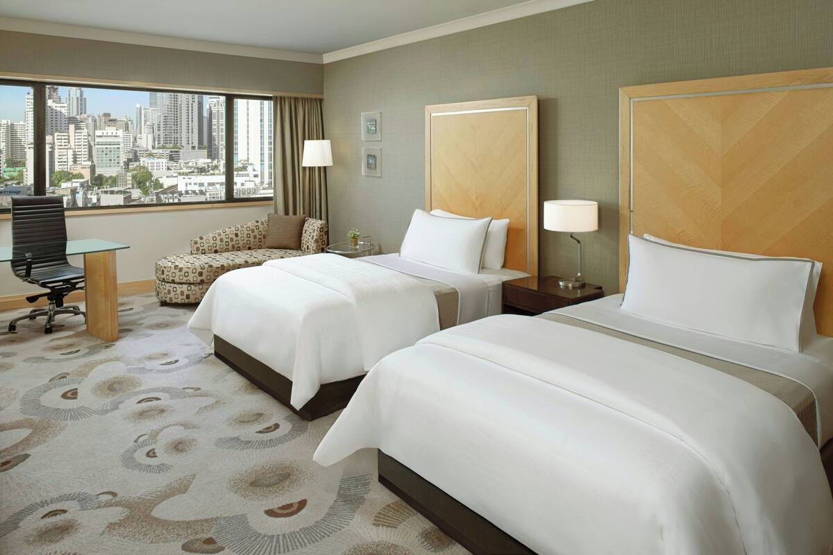 Ein Hotelzimmer mit zwei Betten, Blick auf die Stadt, einem Schreibtisch und einem gemusterten Teppich.