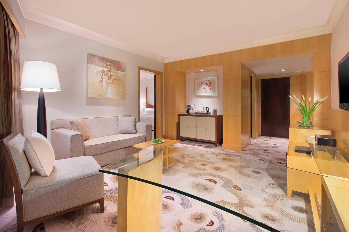 Ein modernes Hotelzimmer mit einer Couch, einem Glastisch, einem Schrank und einem Flachbildfernseher.