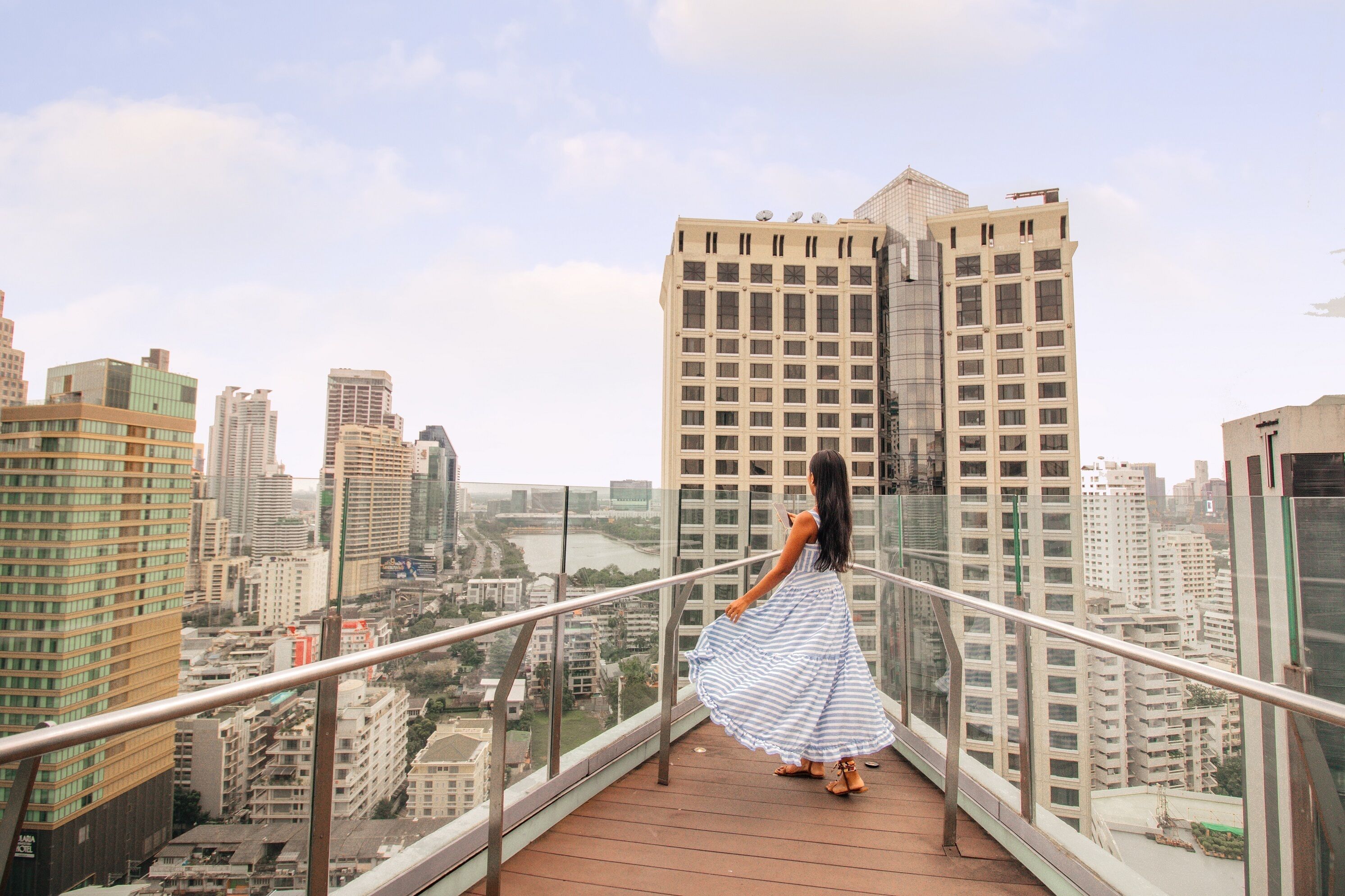 A woman in a blue and white striped dress standing on a balcony with a city view.