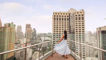A woman in a blue and white striped dress standing on a balcony with a city view.