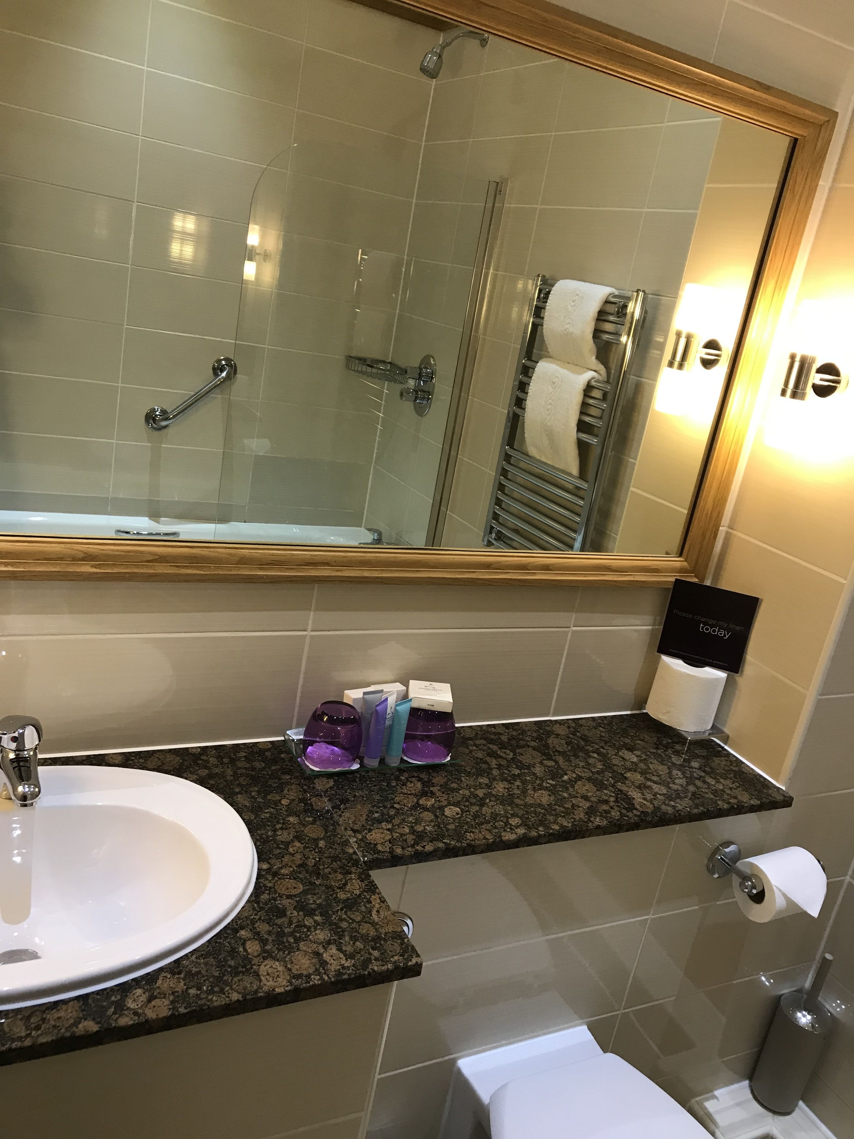A bathroom with a white sink, a mirror, a shower, and a toilet. There are toiletries on the countertop.