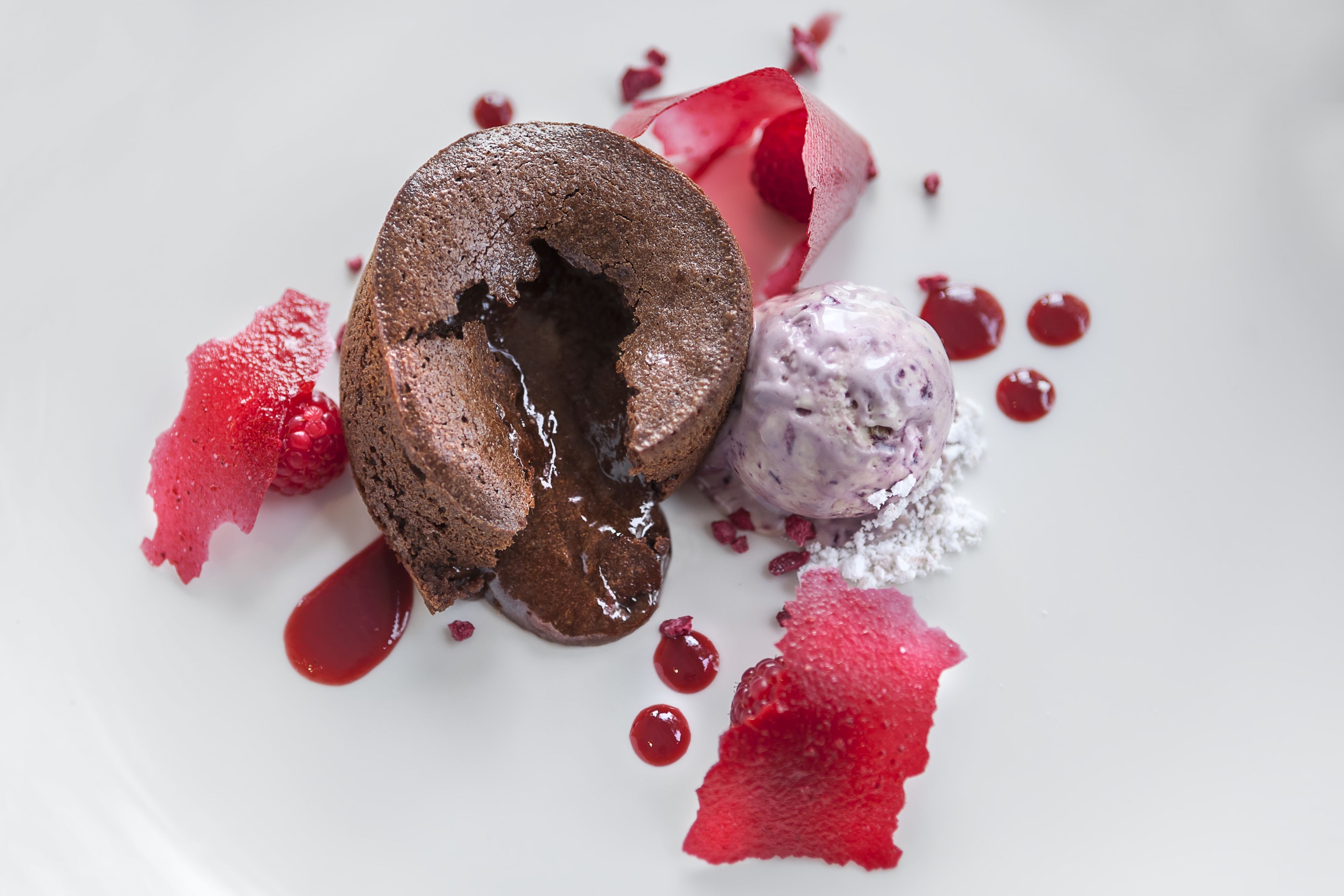 Un plato de postre con un pastel volcán de chocolate, helado y salsa de frutos rojos.