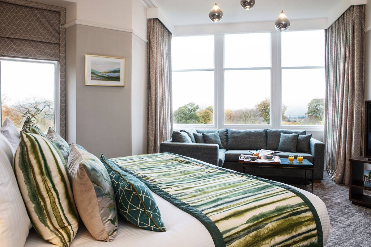 A hotel room with a large bed, a sofa, a dining table, and a TV.