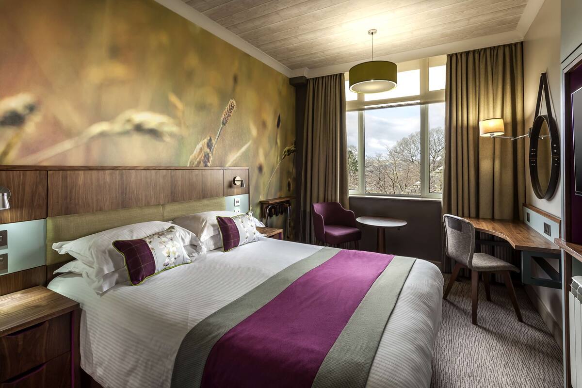 A hotel room with a large bed, a desk, a chair, and a view of the outdoors.