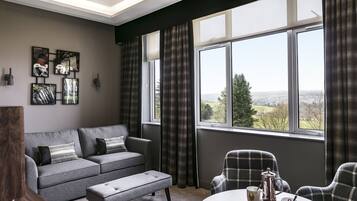 Una sala de estar moderna con un sofá gris, un reposapiés a juego y sillones escoceses. Se observan obras de arte abstracto en la pared y un ventanal con cortinas.