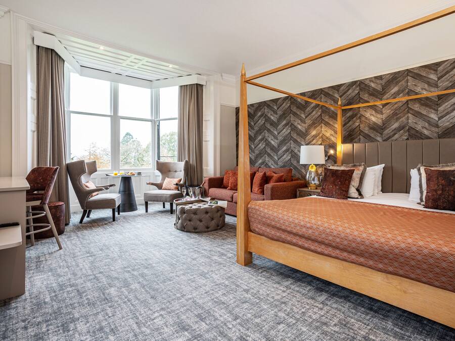 Ein Hotelzimmer mit Himmelbett, einer Couch, einem Schreibtisch und einem Sessel.