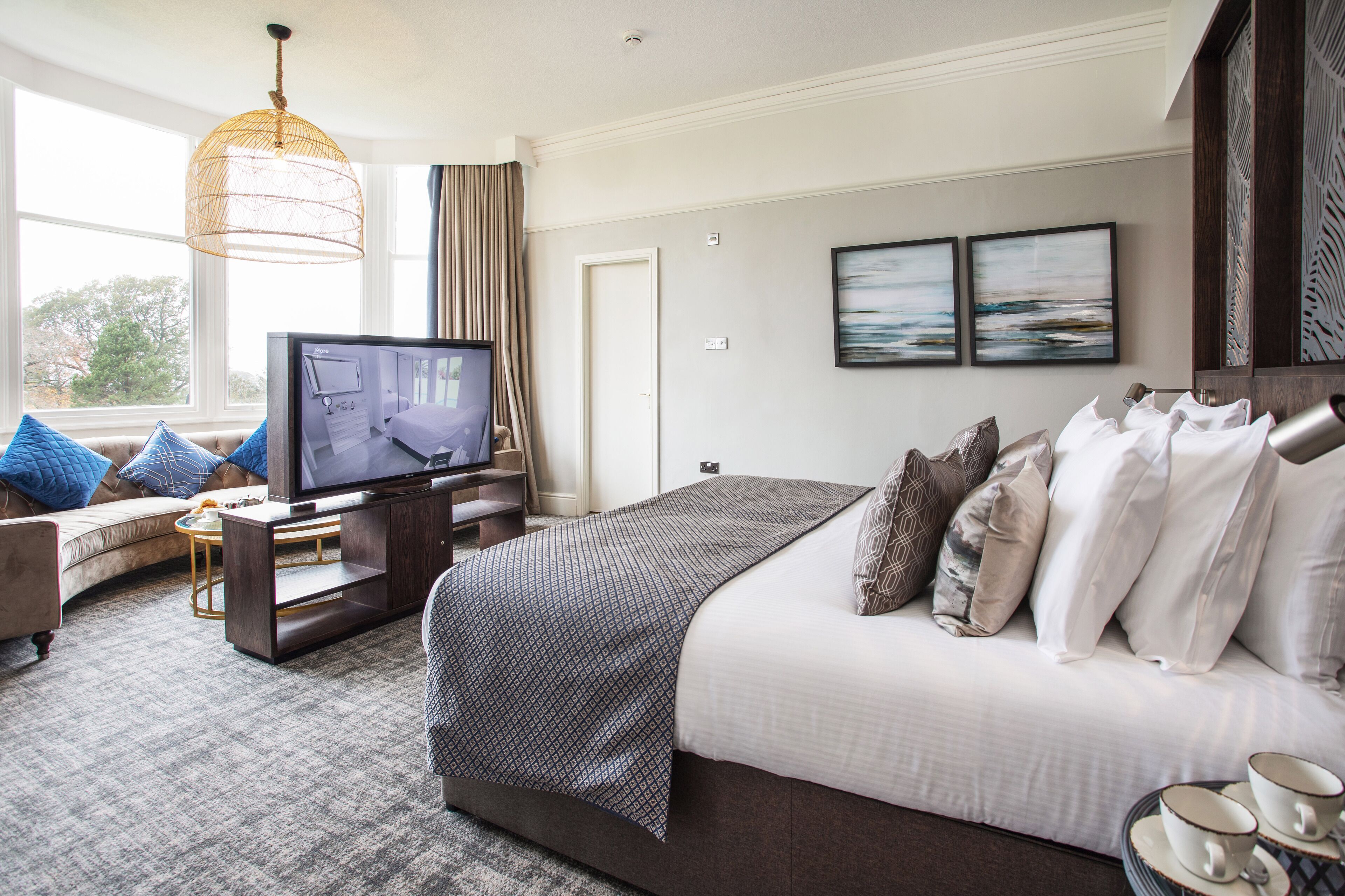 A modern hotel room with a large bed, a television, a sofa, and a view of the outdoors.