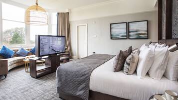 A modern hotel room with a large bed, a television, a sofa, and a view of the outdoors.