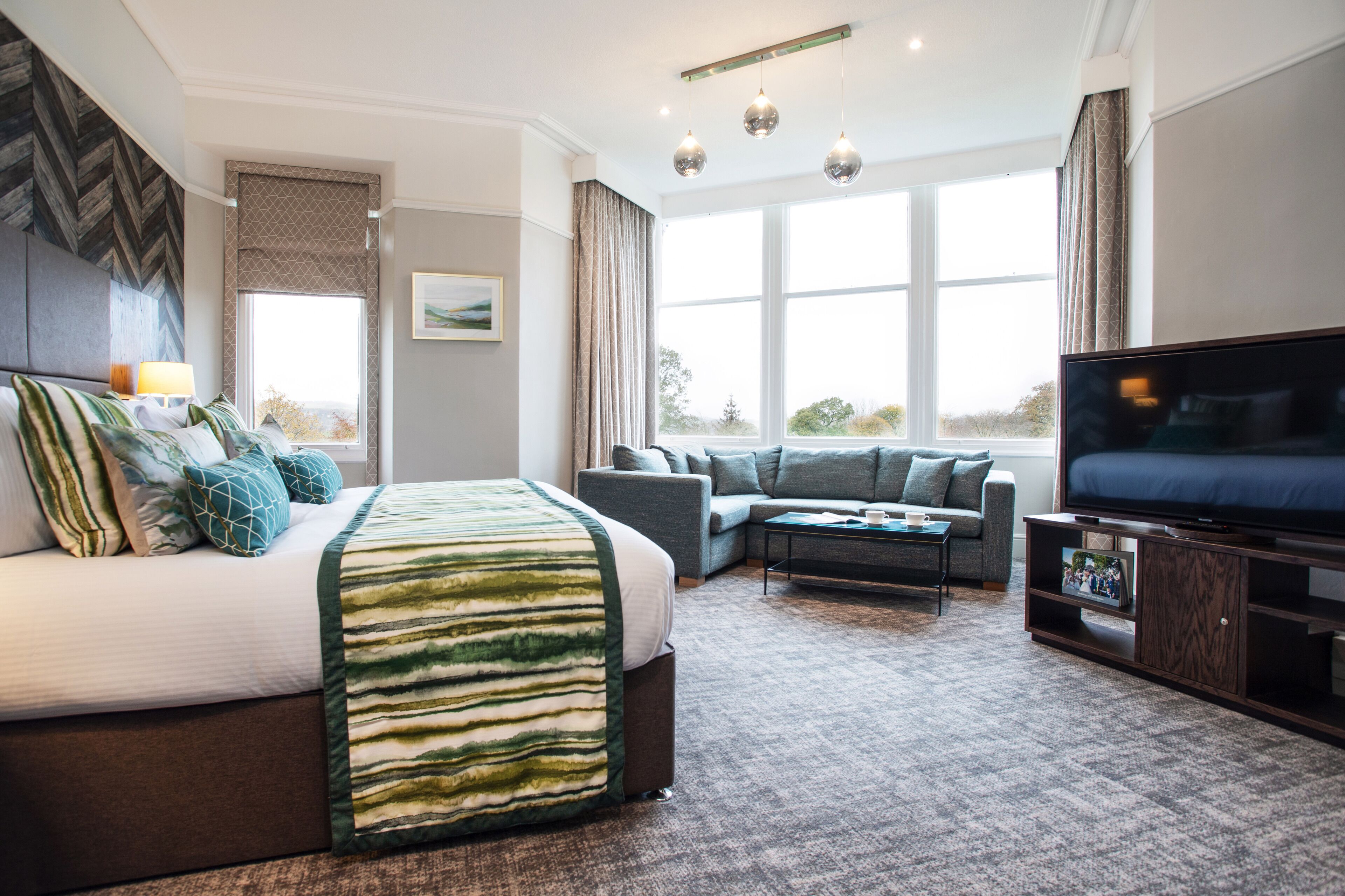Habitación de hotel con una cama grande, un sofá, un televisor y una ventana con cortinas.