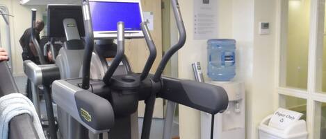 A gym with treadmills, a water dispenser, and a paper-only trash bin.