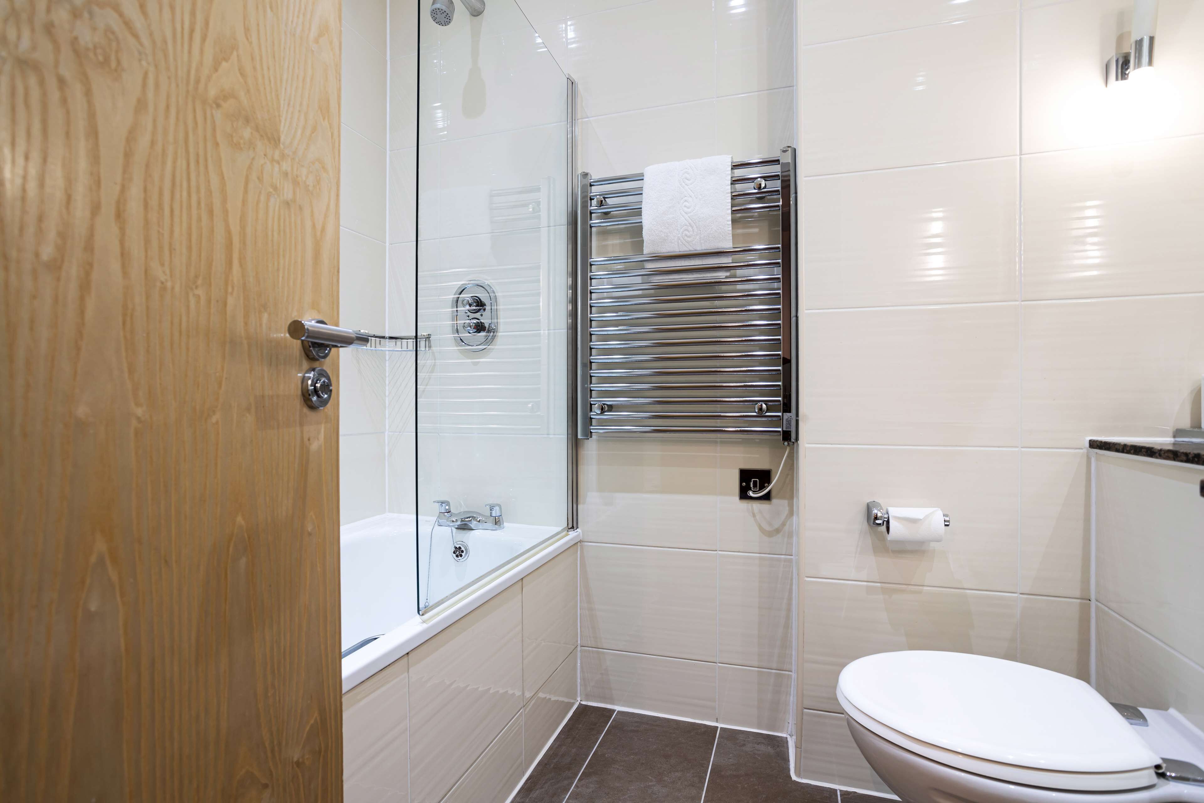 A bathroom with a glass shower enclosure, a white toilet, and a towel rack.