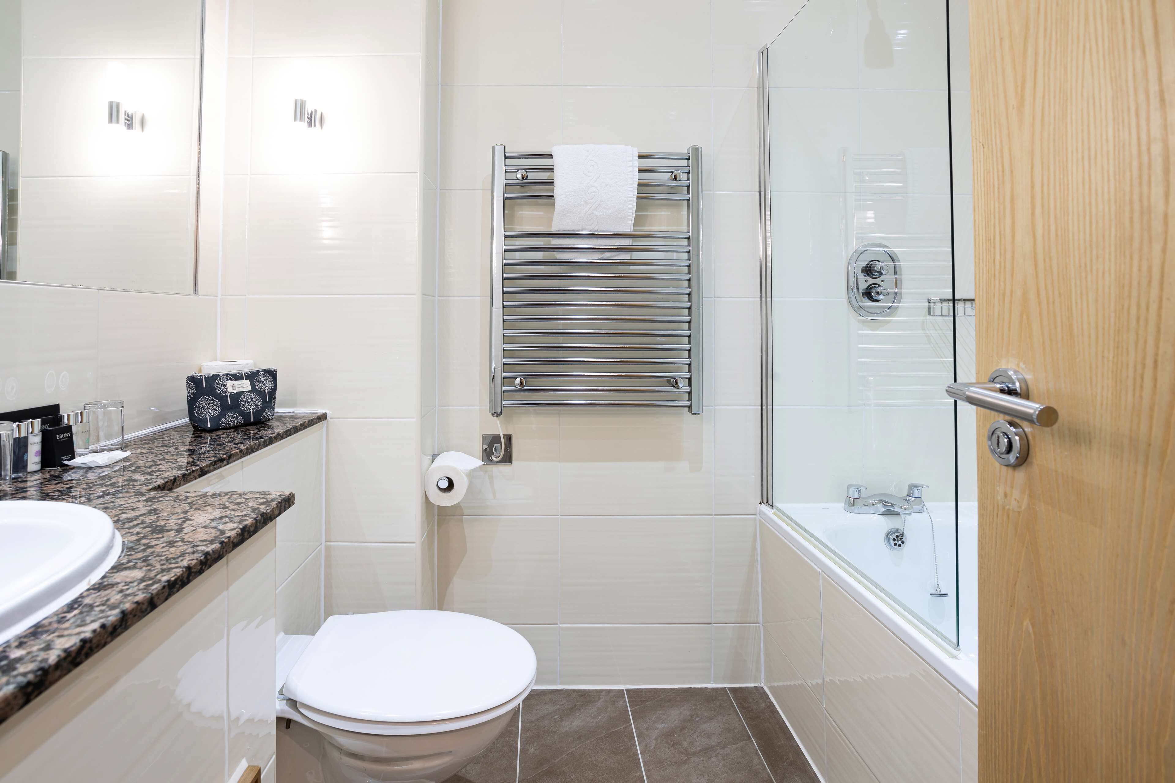A modern bathroom with a marble countertop, a toilet, a towel rack, a glass shower enclosure, and a wooden door.