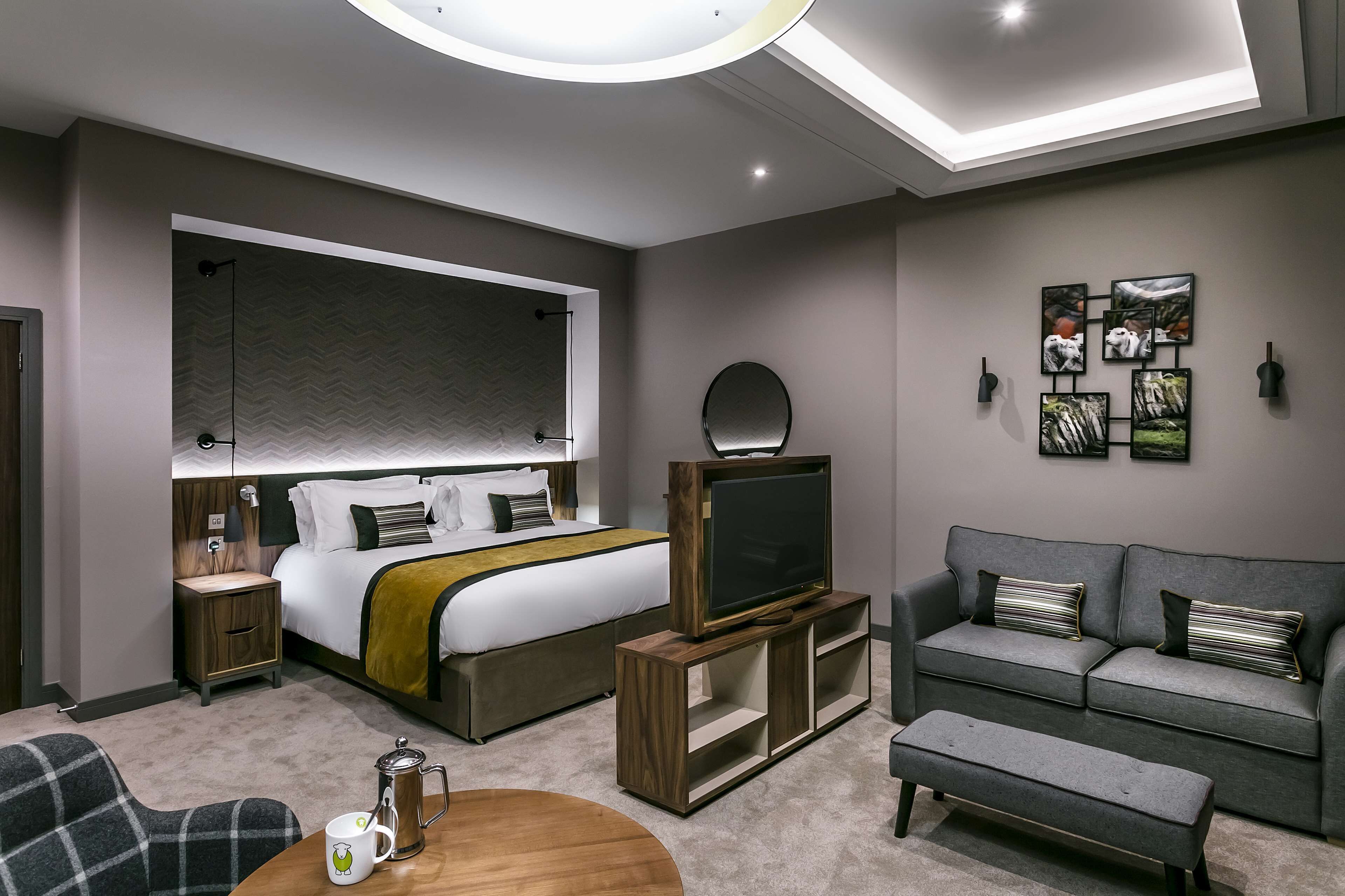 A modern hotel room with a bed, sofa, TV, and artwork on the wall.