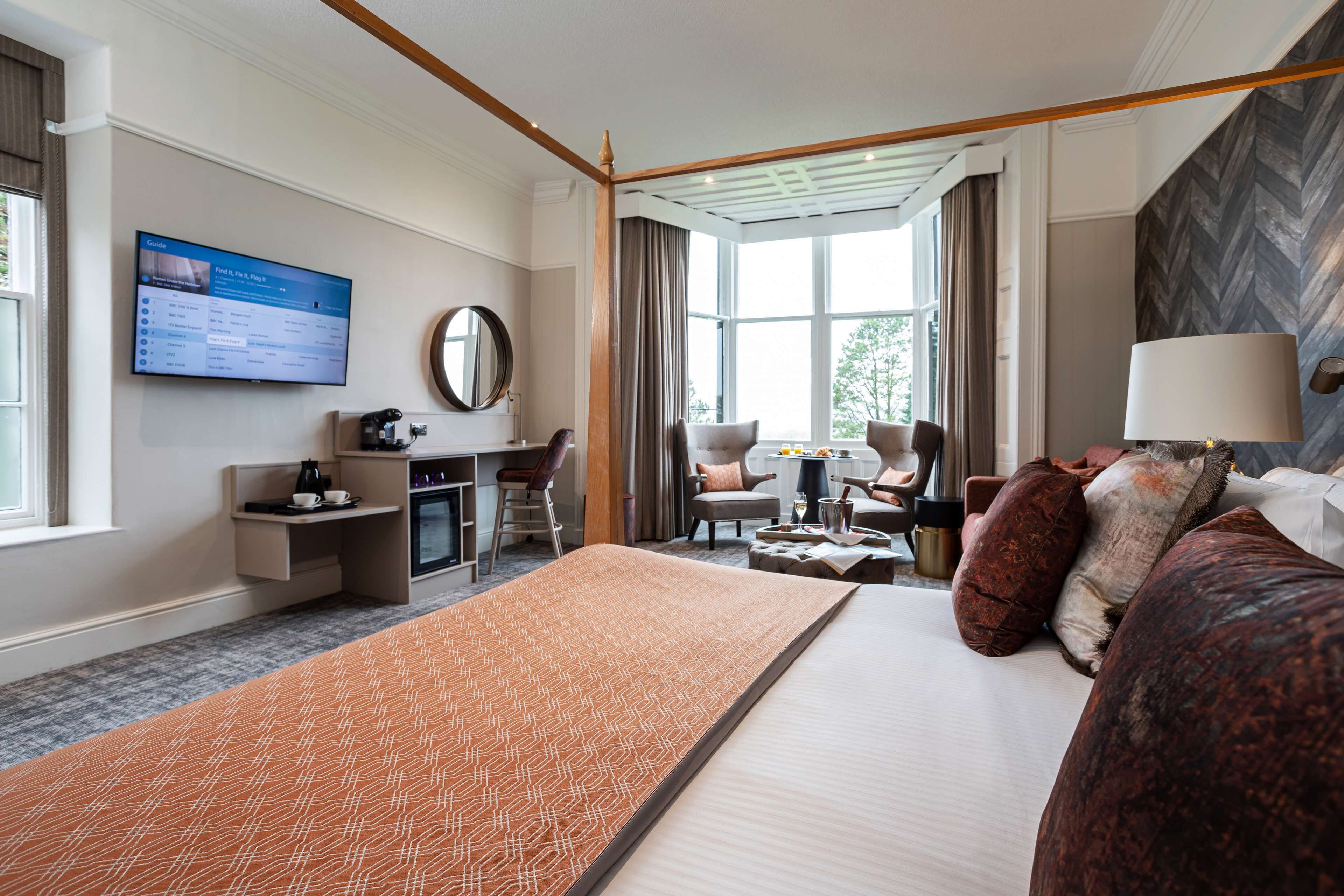 Habitación de hotel con una cama grande, un escritorio, una silla, televisión y vistas al exterior.