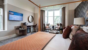 Habitación de hotel con una cama grande, un escritorio, una silla, televisión y vistas al exterior.
