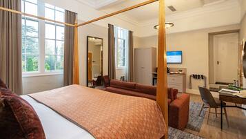 A hotel room with a four-poster bed, a desk, a chair, a sofa, and a television.