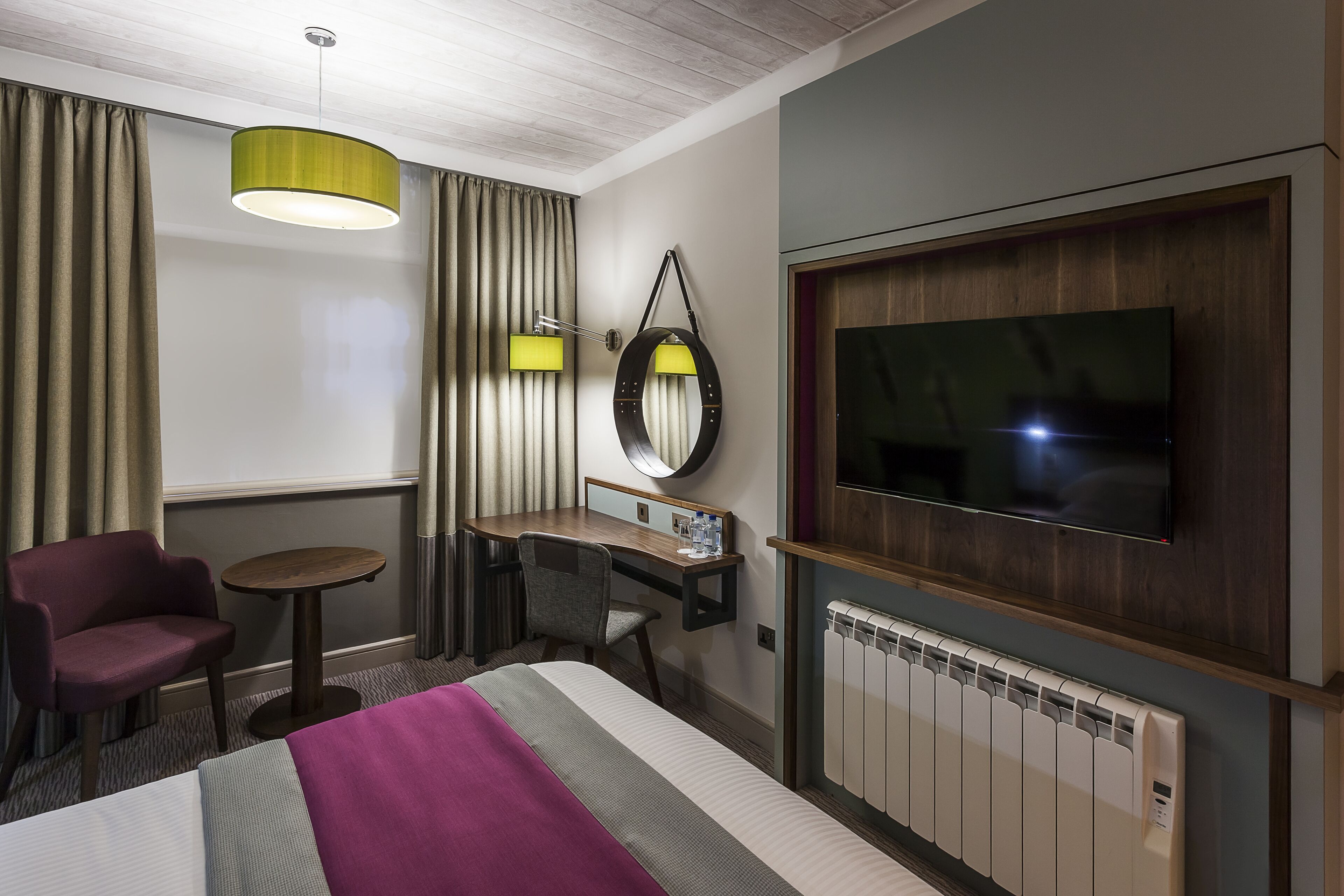 Habitación de hotel con cama, escritorio, silla, televisor y ventana con cortinas.