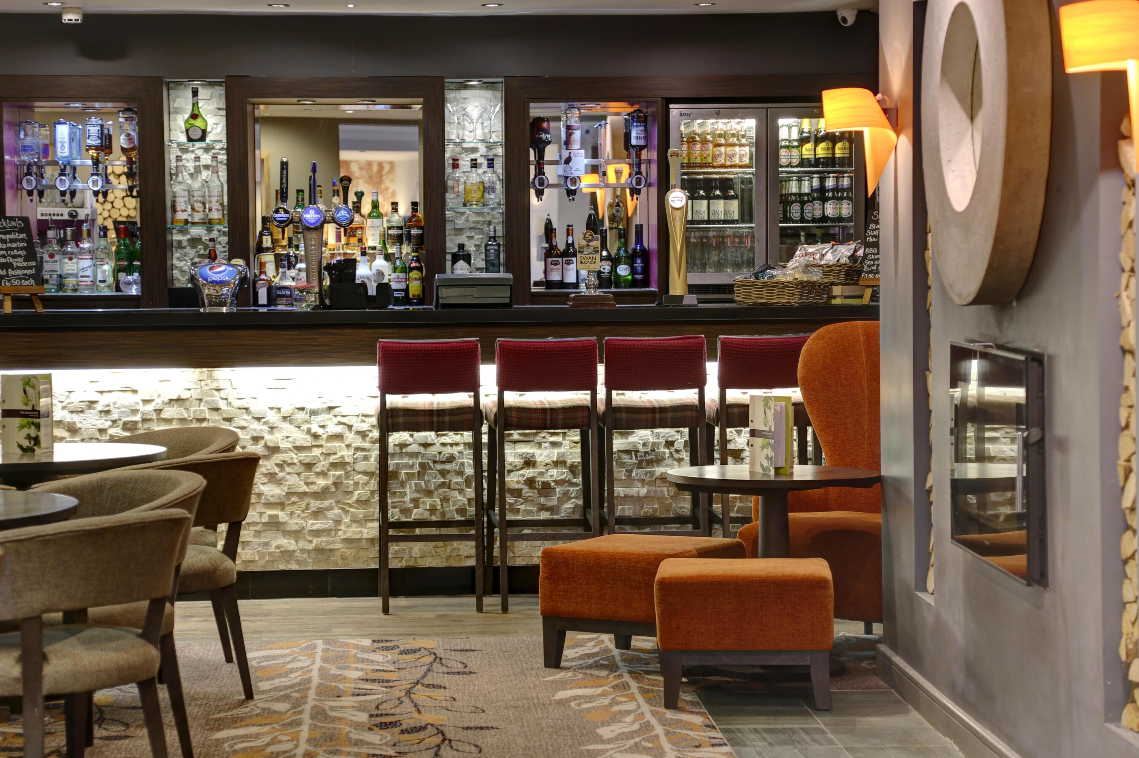 A bar area with stools, a counter with bottles, and a stone wall.