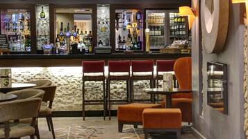 A bar area with stools, a counter with bottles, and a stone wall.