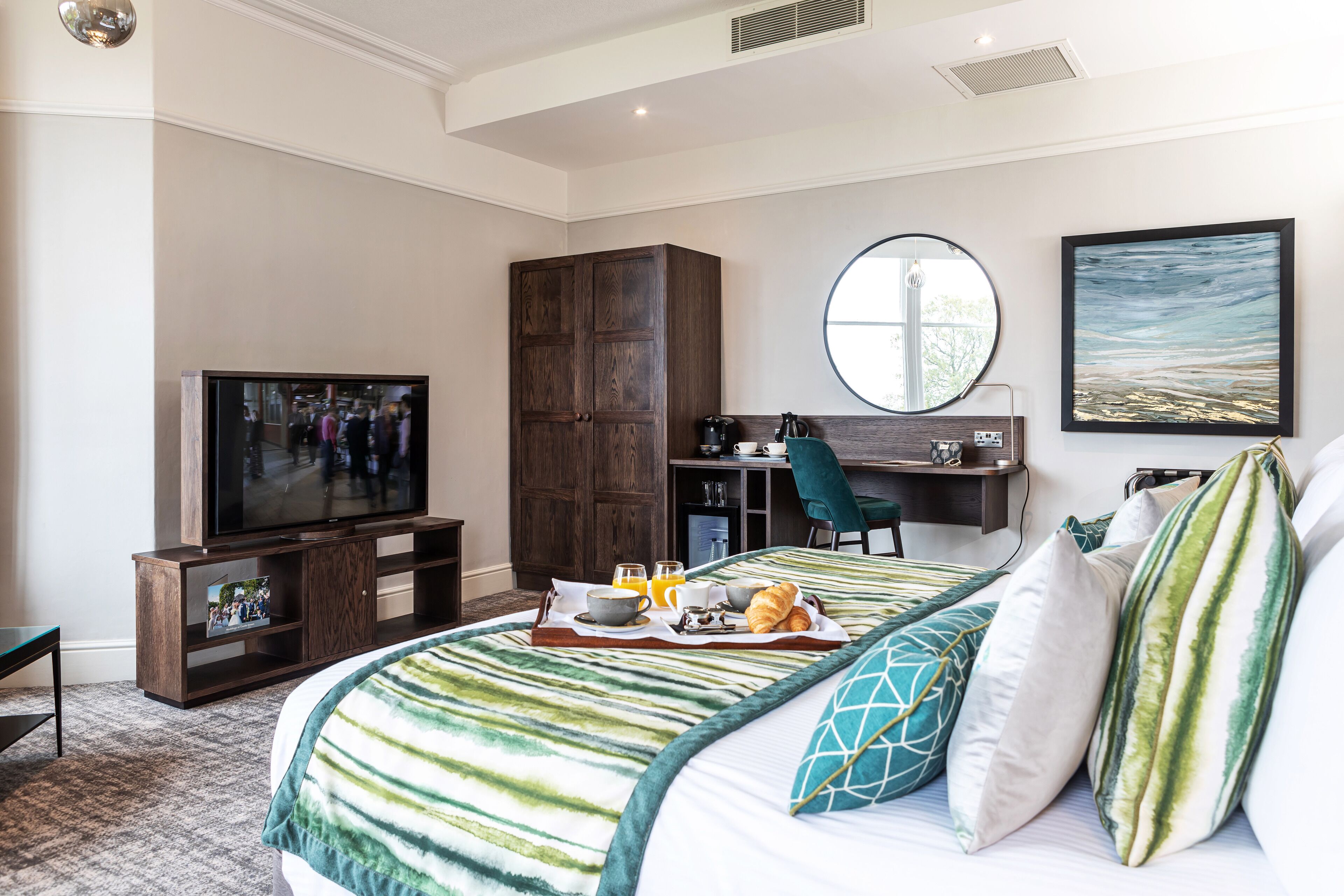 A hotel room with a large bed, a TV, a desk with a chair, and a breakfast tray on the bed.