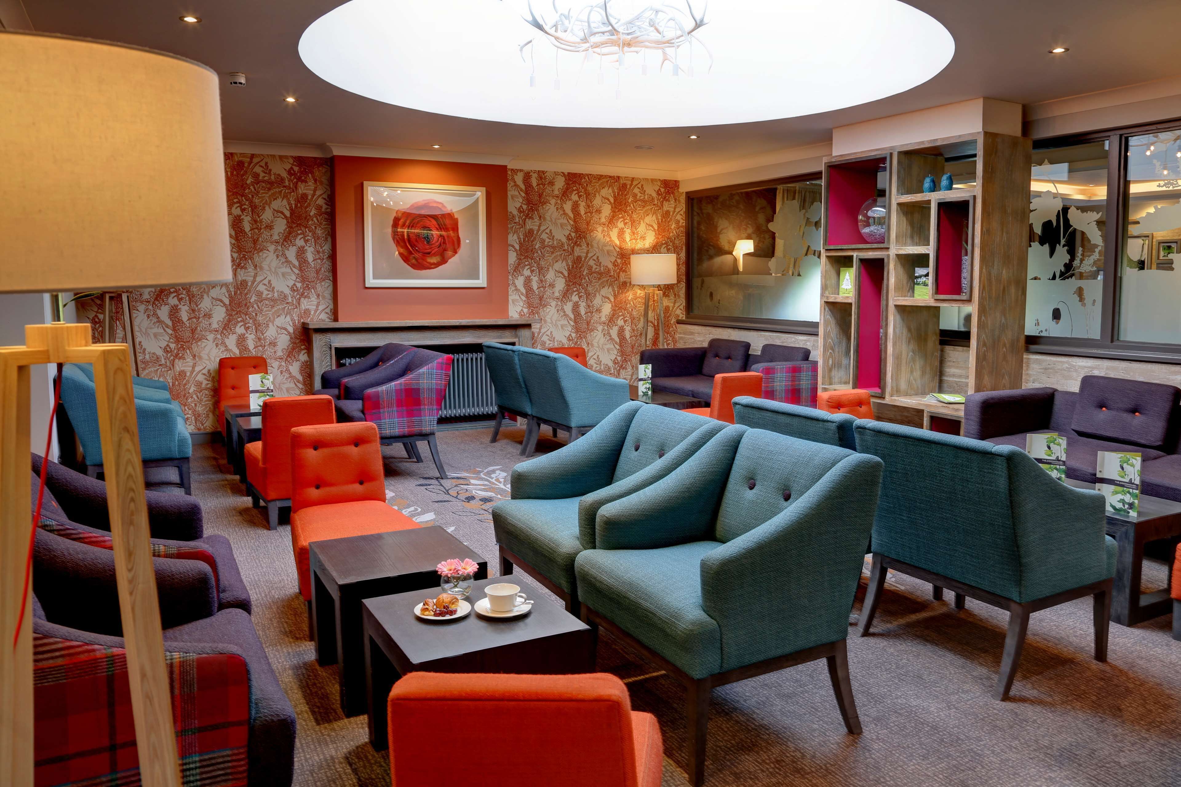 Un área de lounge moderna con varias opciones de asientos, incluyendo sofás y sillones, dispuestos alrededor de una chimenea central.