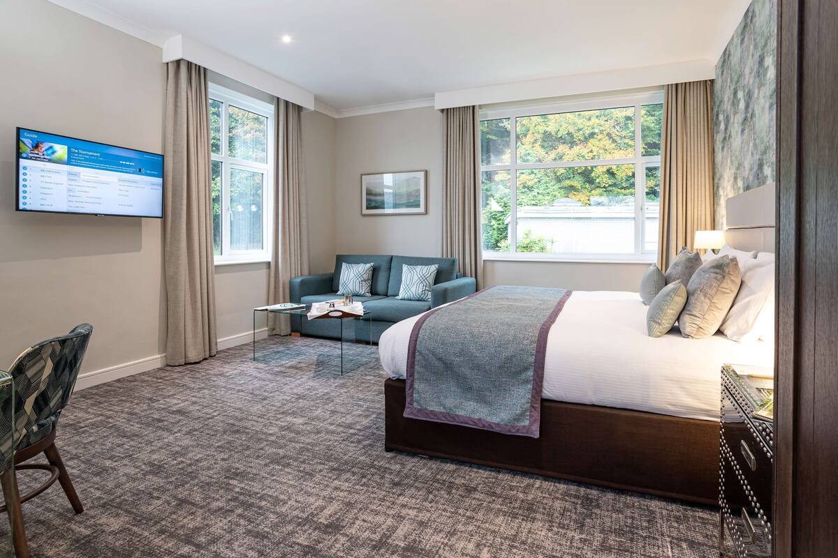 A hotel room with a large bed, a sofa, a TV mounted on the wall, and a window with curtains.