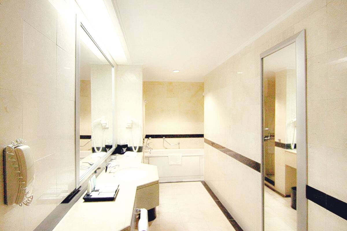 Une salle de bain moderne avec un grand miroir, une baignoire et un meuble-lavabo doté d’un porte-serviettes.