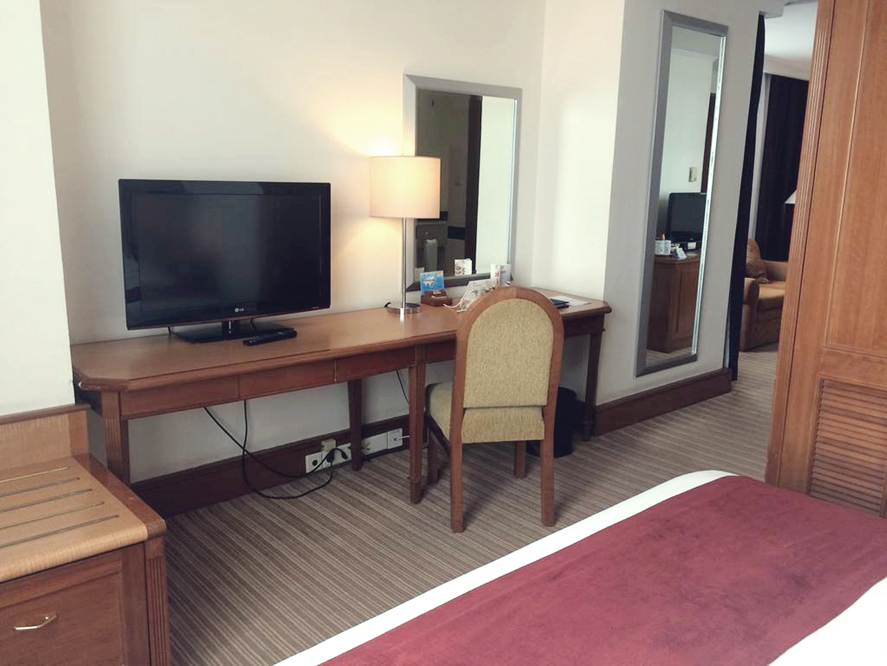 Una habitación de hotel con una cama, un escritorio con televisor, una silla, una lámpara y un espejo.