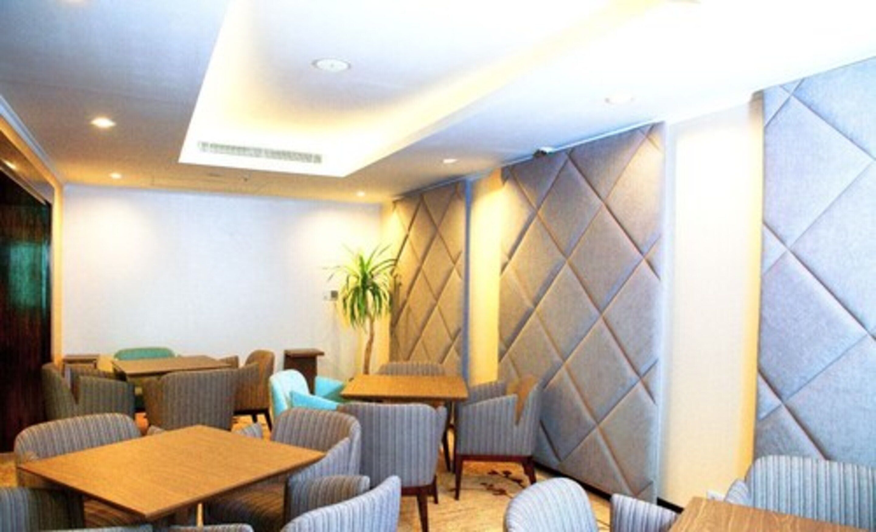 Un vestíbulo de hotel con asientos acolchados, mesas y una pared decorativa.