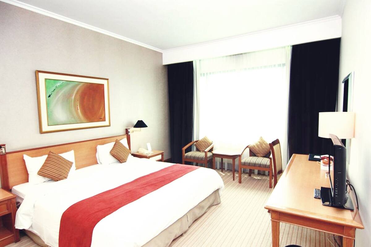 Une chambre d’hôtel avec un grand lit, deux tables de chevet, un bureau avec une chaise, une télévision et une fenêtre avec des rideaux.