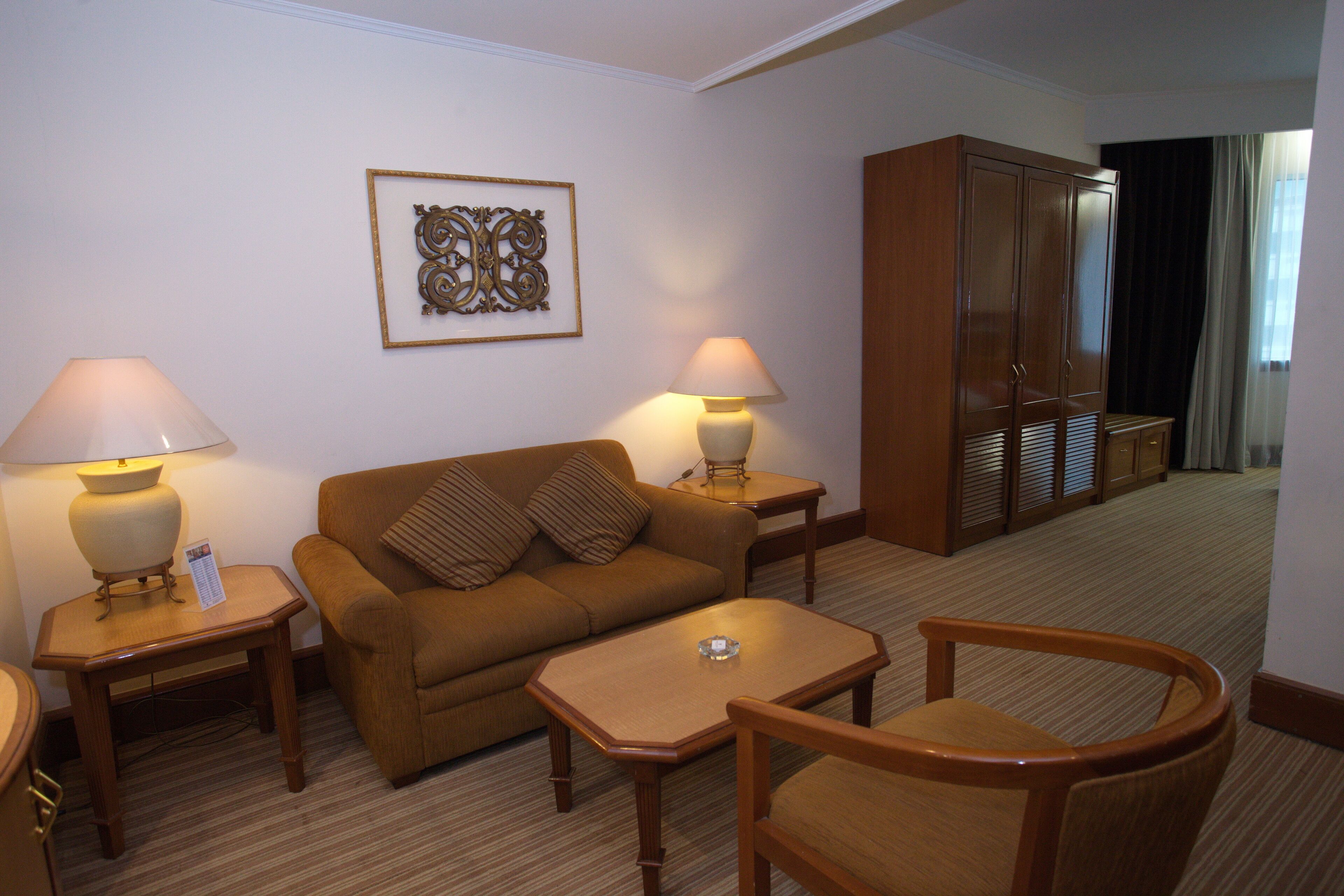 A hotel room with a brown sofa, two lamps, a small table, and a wooden wardrobe.