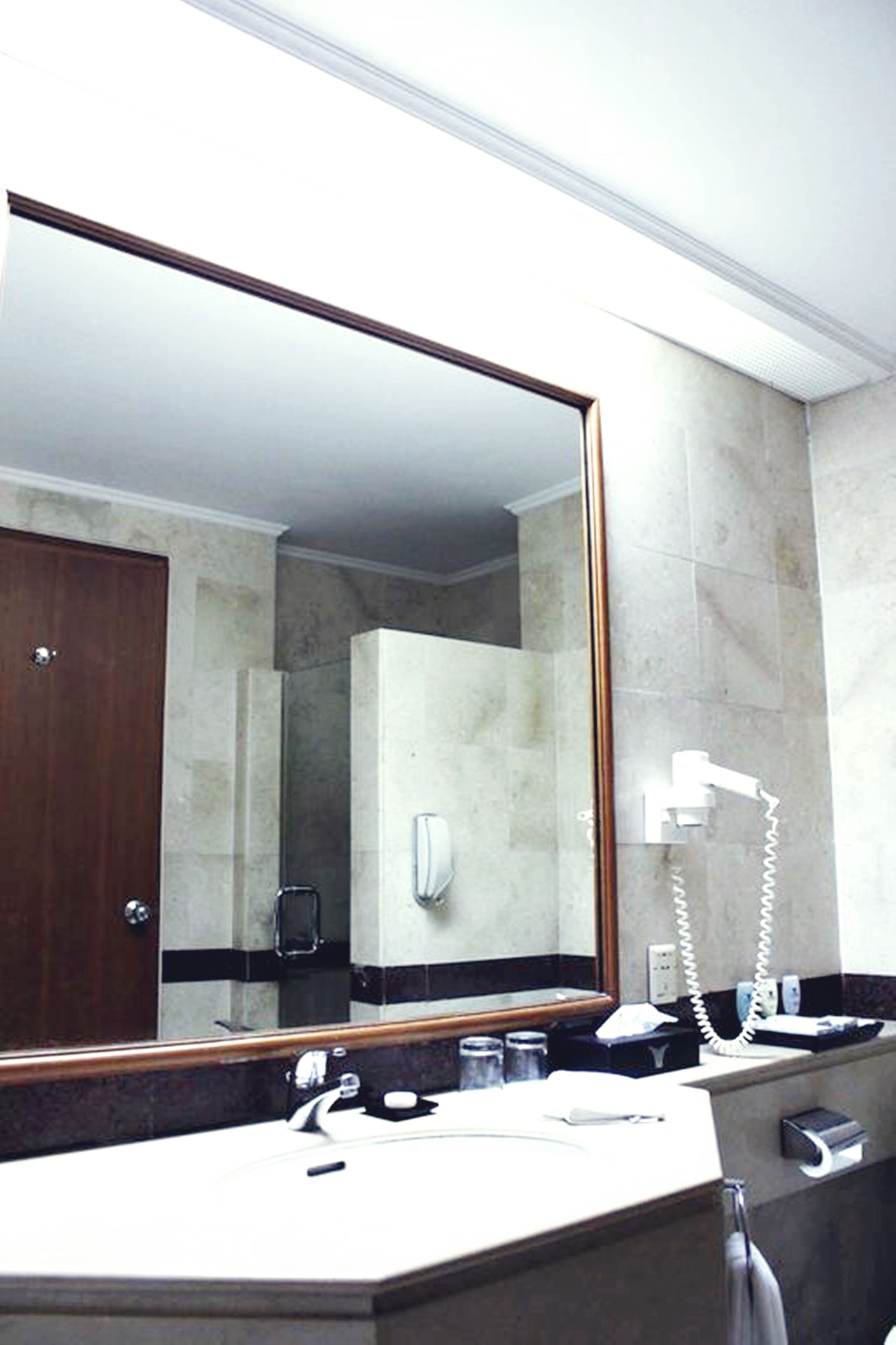 Een hotelbadkamer met een grote spiegel, een wastafel, een haardroger en een telefoon.
