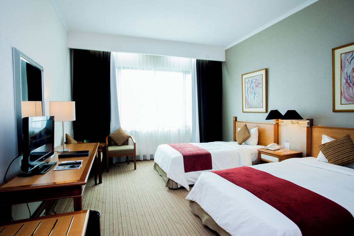 Une chambre d’hôtel avec deux lits, un bureau avec une télévision, une chaise et une fenêtre avec des rideaux.