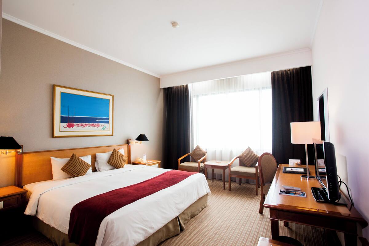 Une chambre d’hôtel avec un grand lit, un bureau avec un ordinateur, une chaise, une petite table et un téléviseur.