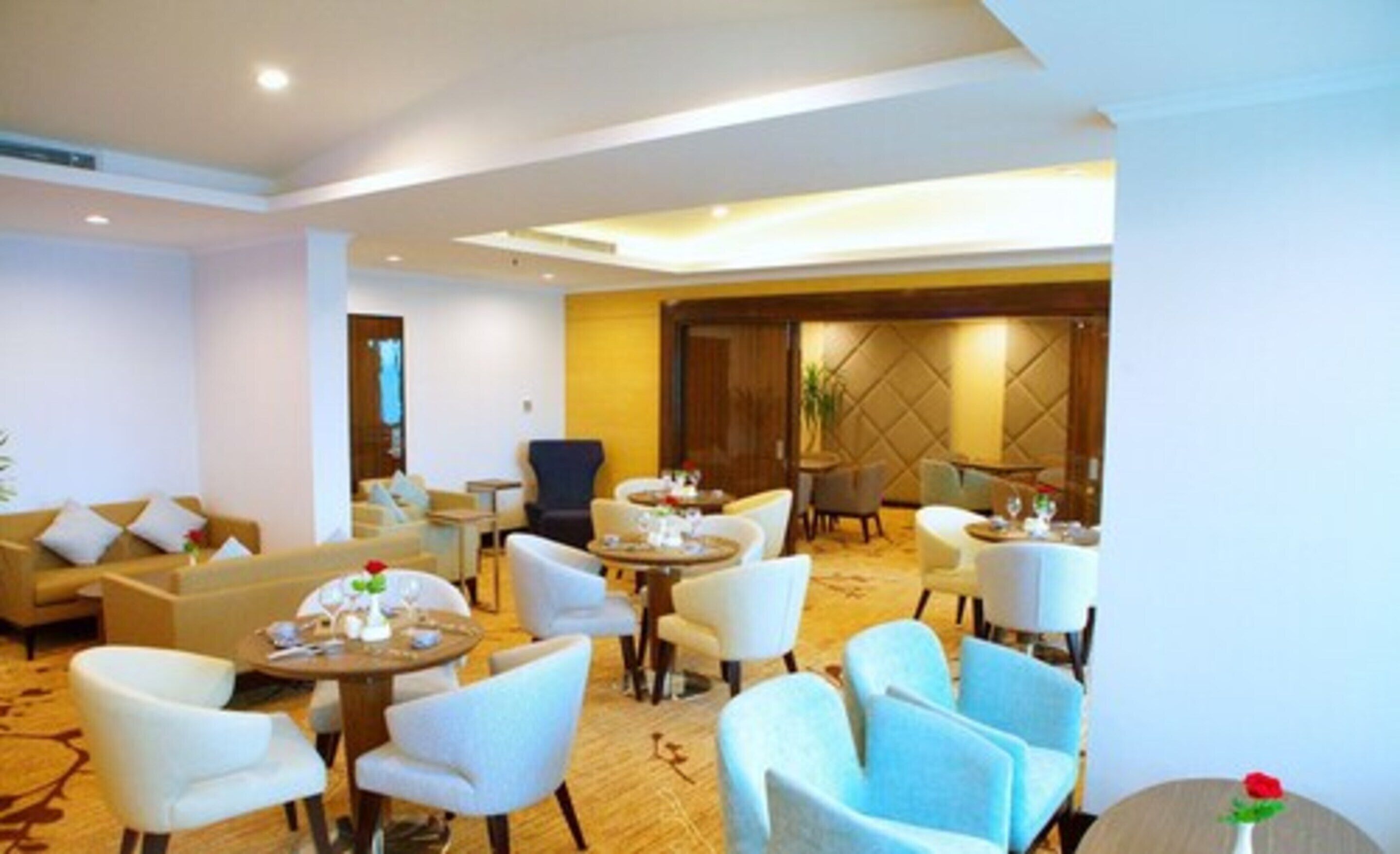 En hotelllobby med flera sittgrupper, inklusive soffor och runda bord, och ett stort fönster som släpper in naturligt ljus.