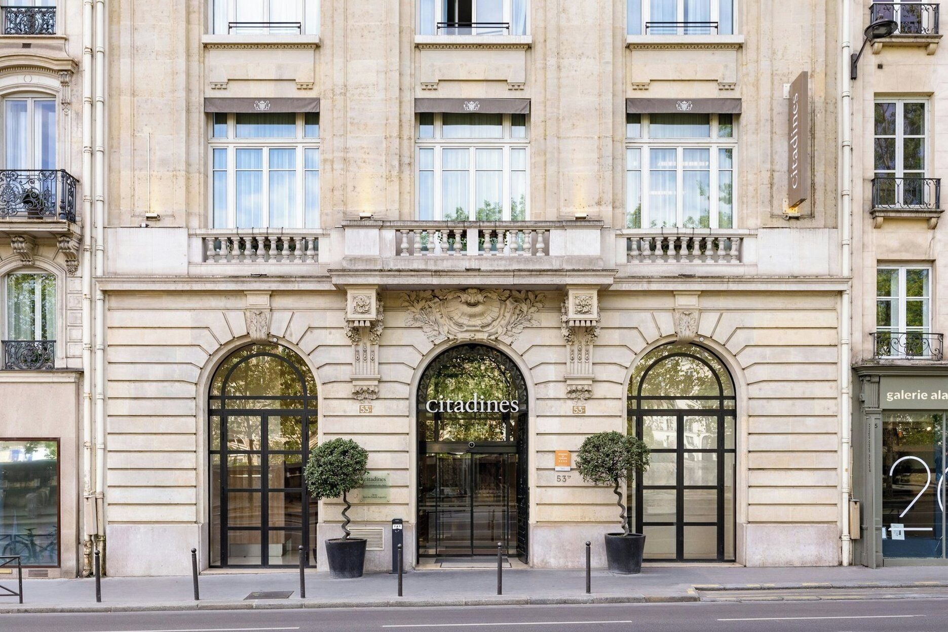 Une façade de style classique, dotée de trois entrées en arc de cercle, d’un élément décoratif central et d’une enseigne indiquant « Citadines ».