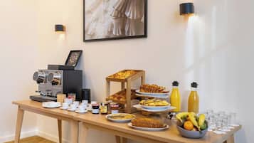 Un buffet de petit-déjeuner avec des machines à café, des viennoiseries, des fruits et des bouteilles de jus.