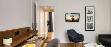A modern living room with a wooden console table, a grey armchair, a white side table, and a black sofa.