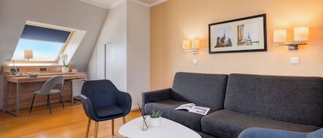 A modern room with a desk, two chairs, a grey sofa, a small white table, and a picture on the wall.
