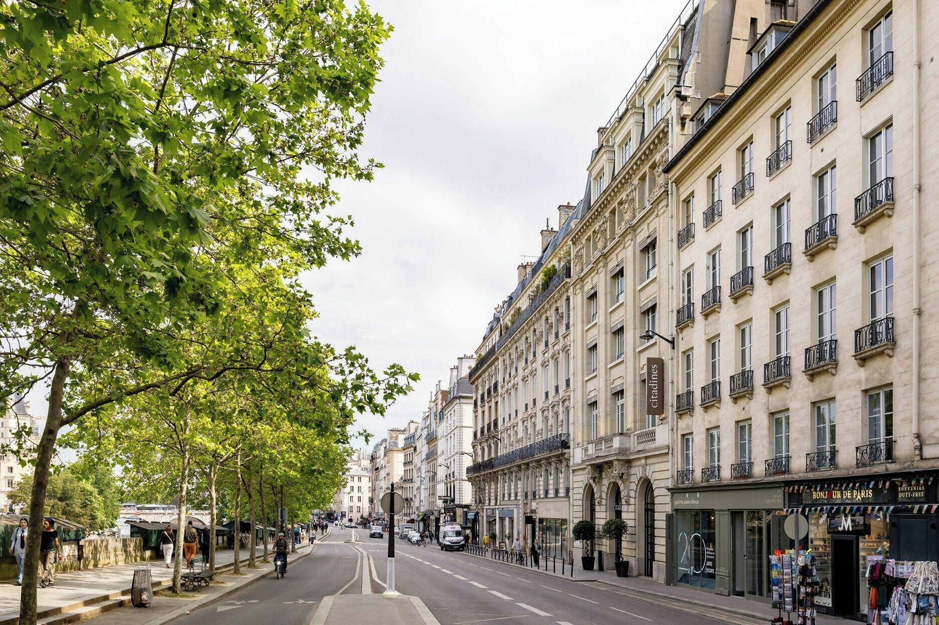 A tree-lined street with historic buildings, a Citadines hotel, and a store named BONJOUR DE PARIS.